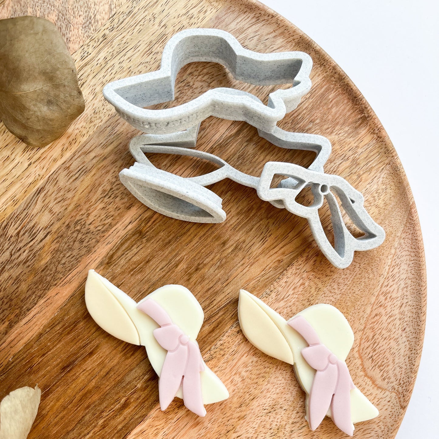 Cookie cutter shaped like a bunny with a bow on a wooden board with shaped cookies.