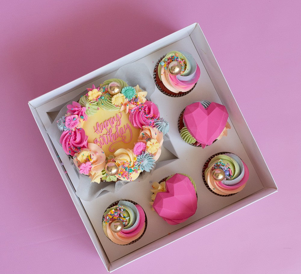 Box of colorful birthday cupcakes on a pink background