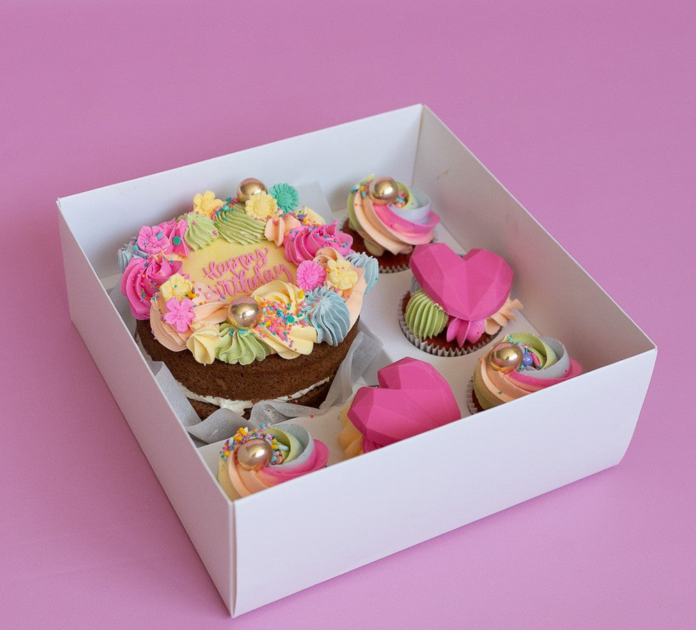 Decorative birthday cake with colorful icing in a white box on a pink background