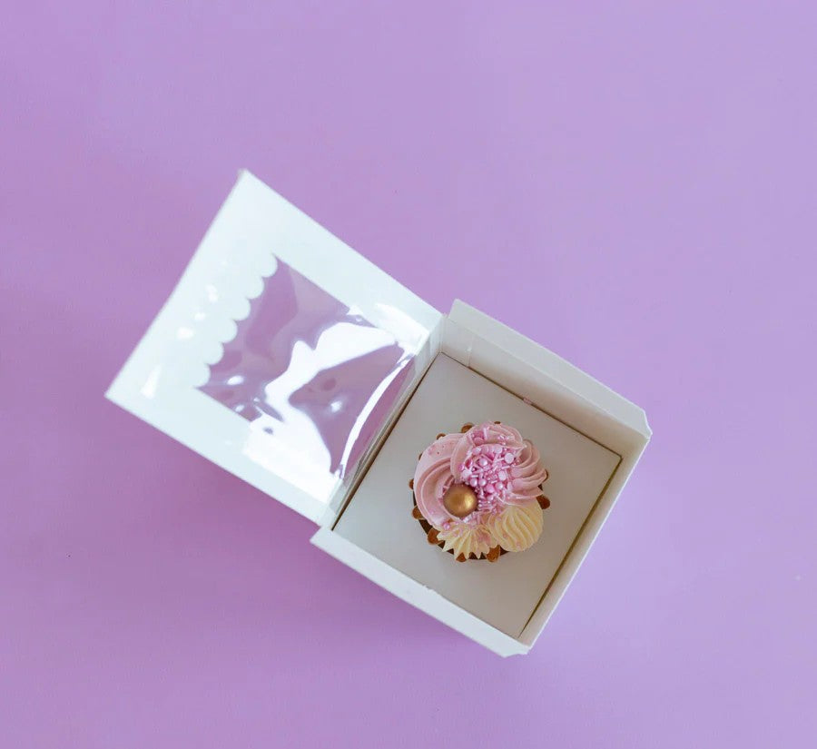 Cupcake with pink frosting in a white box on a purple background
