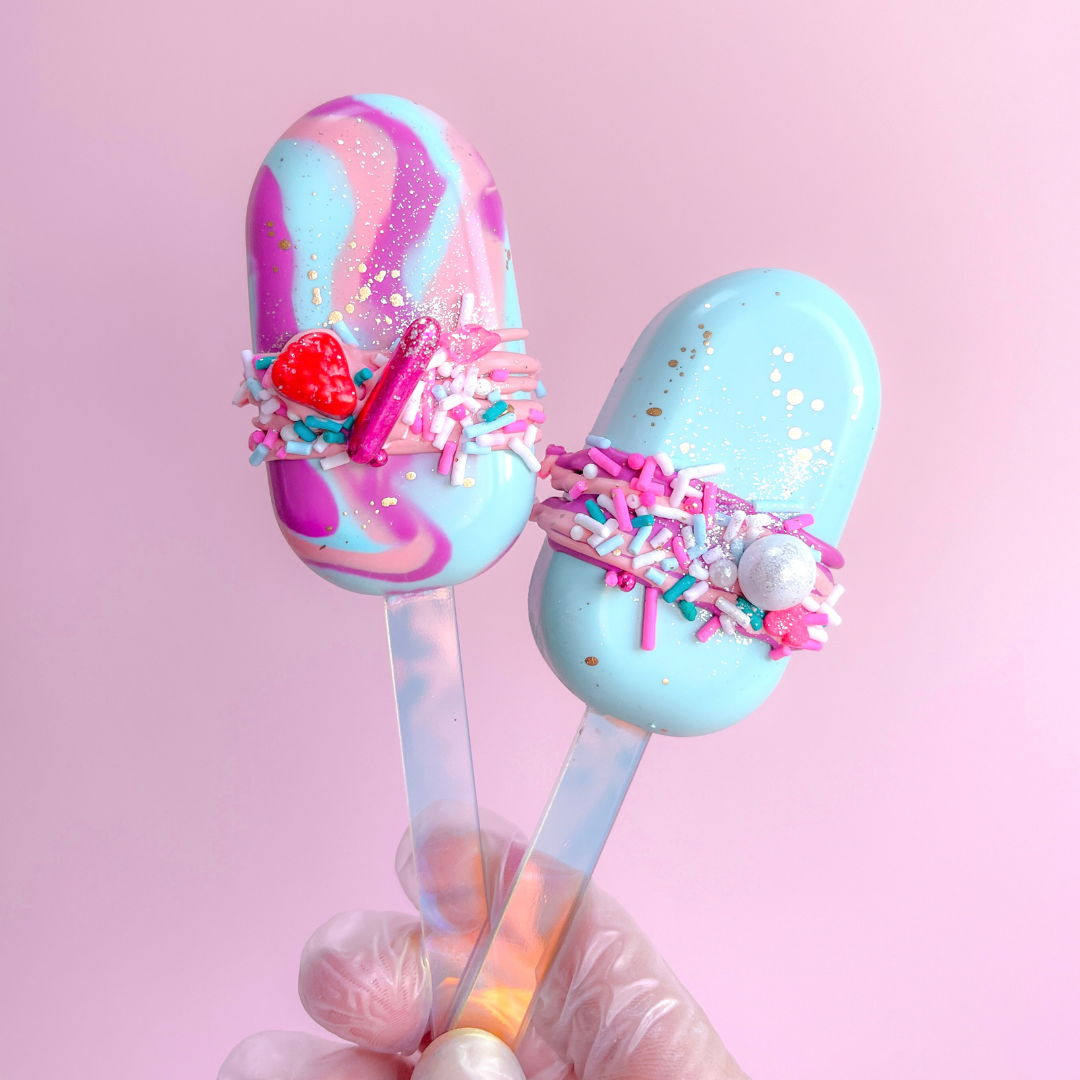 Two colorful dessert spoons with sprinkles against a pink background