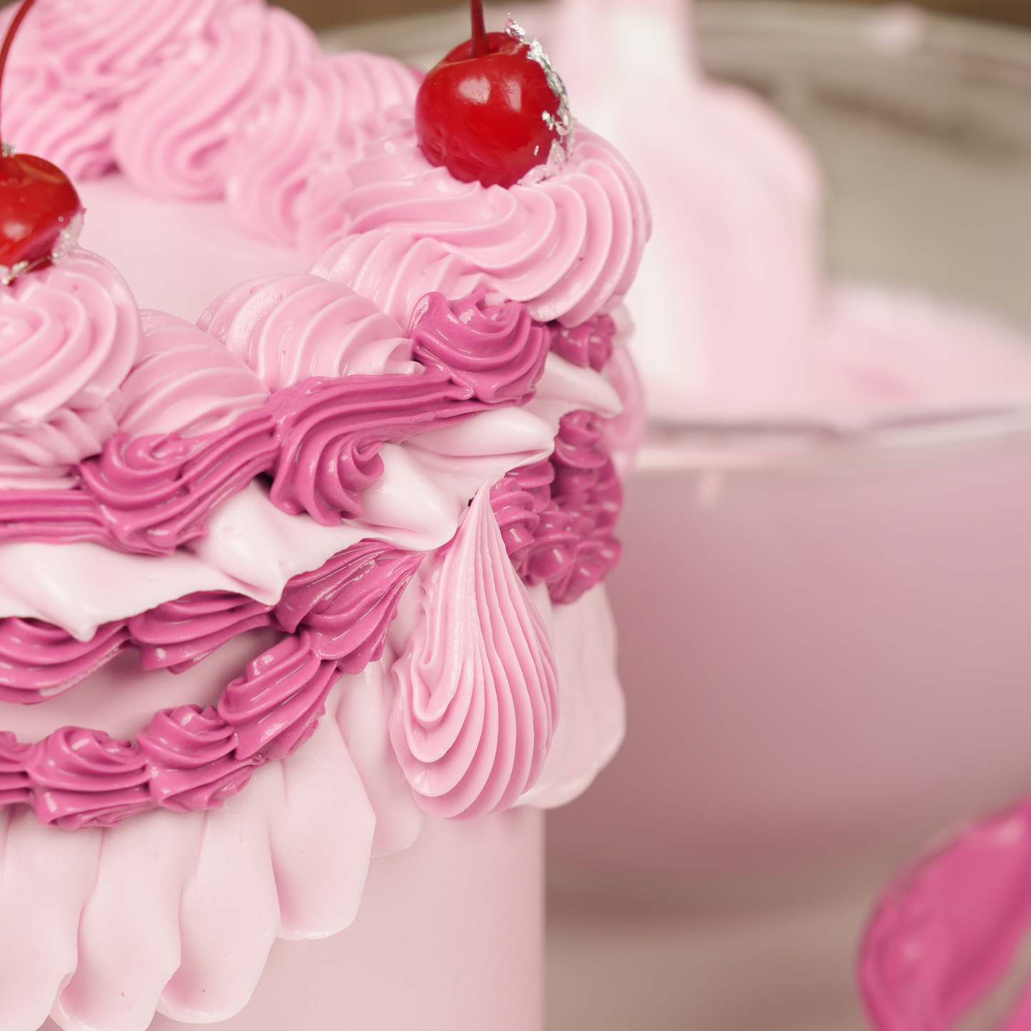 Close-up of a pink cake with white frosting and red cherries on top.