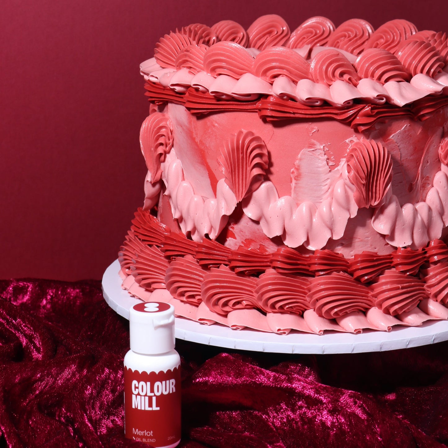 Red and pink cake with decorative patterns on a red background, accompanied by a bottle of Colourfulill.