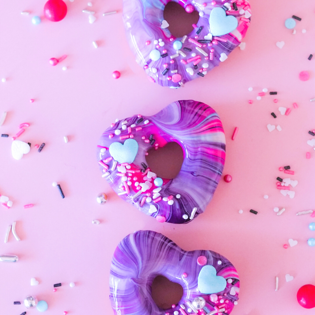 Colorful heart-shaped donuts with sprinkles on a pink background