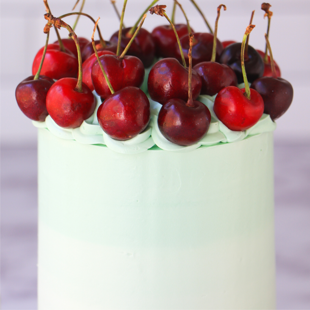 Green frosted cake with red cherries on top against a blurred background