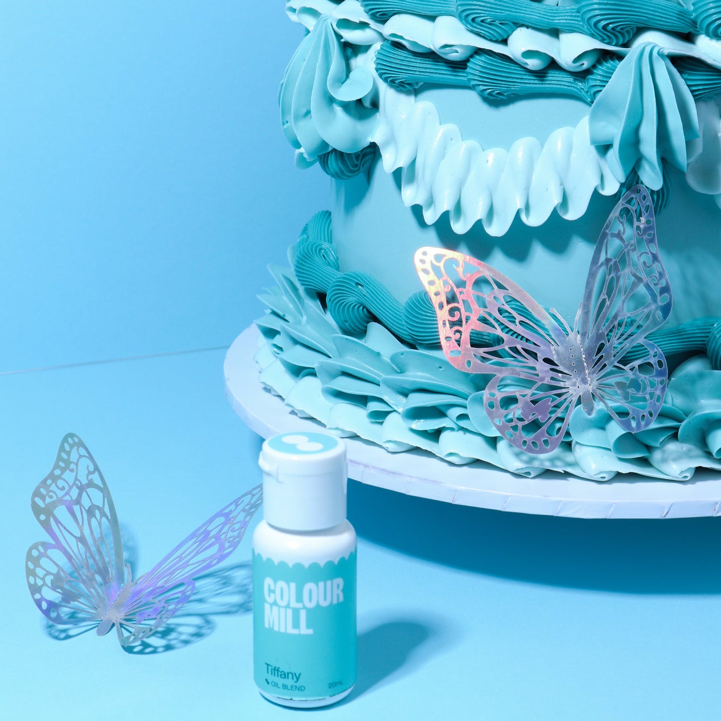 Teal cake with decorative butterflies and a bottle of Colourful icing on a blue background