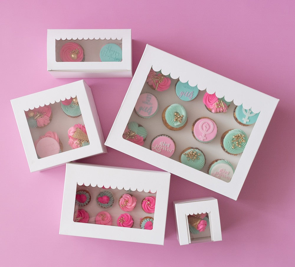 Set of white display boxes with small cakes on a pink background