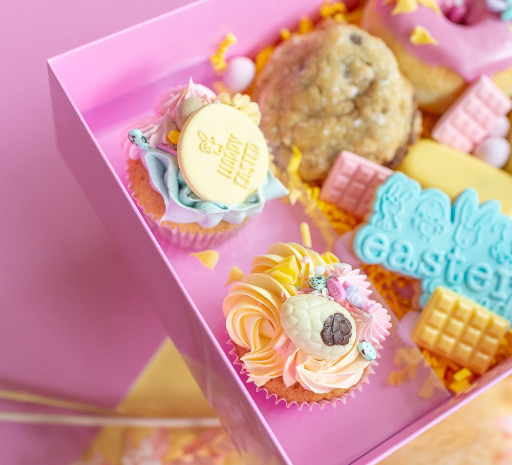 Pastel-colored Easter-themed cupcakes and cookies in a pink box.