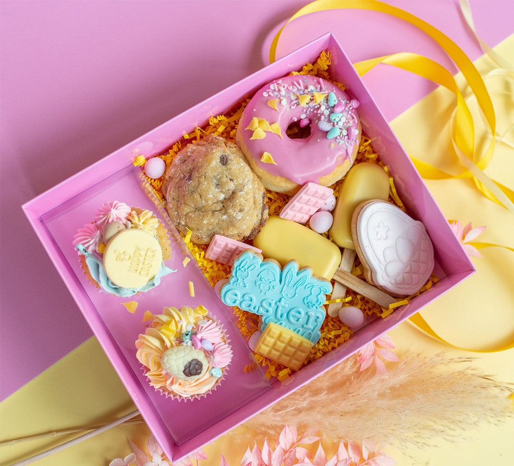 Box of Easter-themed cookies with pink icing and decorative elements on a pink background.