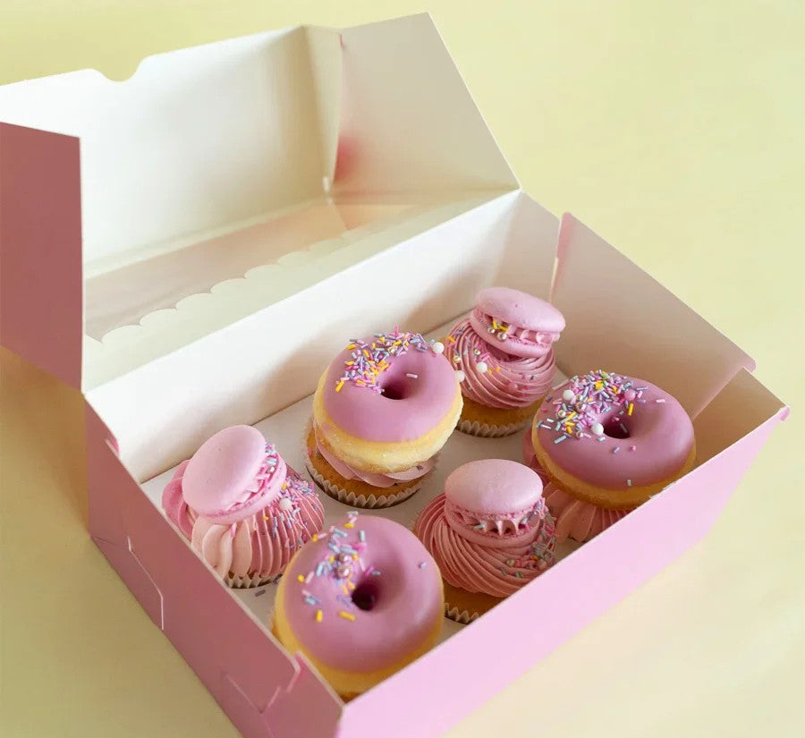 Box of pink and pastel donuts with sprinkles on a light yellow background