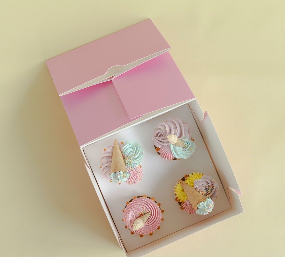 Decorative cupcakes in a pink box on a light yellow background