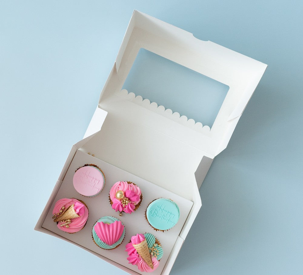 Box of colorful mini cakes with ice cream cone design on a light blue background