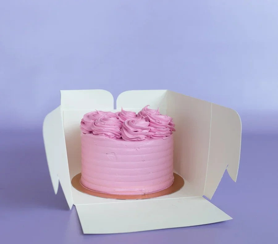 Pink frosted cake with rosettes in a white box on a purple background