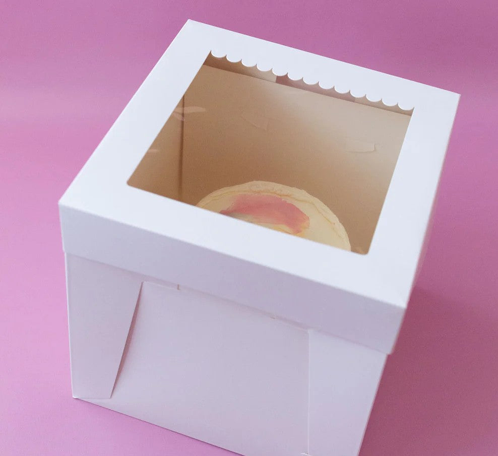 White cake box with a clear window on a pink background