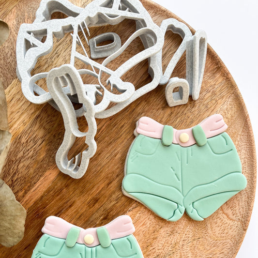 Cookie cutters shaped like green shorts with pink collars on a wooden board.