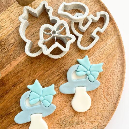 Set of cookie cutters shaped like pacifiers and bows on a wooden board.