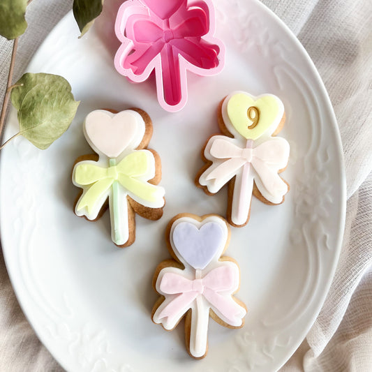 Heart-shaped cookie cutter on a stick with bow detail, perfect for cute cookies for parties, Valentine’s Day, or birthdays.