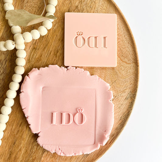pink embossed cookie stamp with 'IDO' branding on a wooden tray.