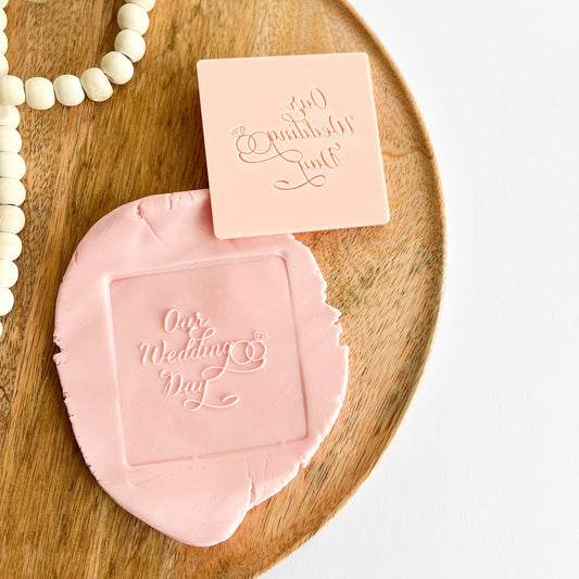 Pink embossed stamp with 'Our Wedding Day' text on a wooden tray