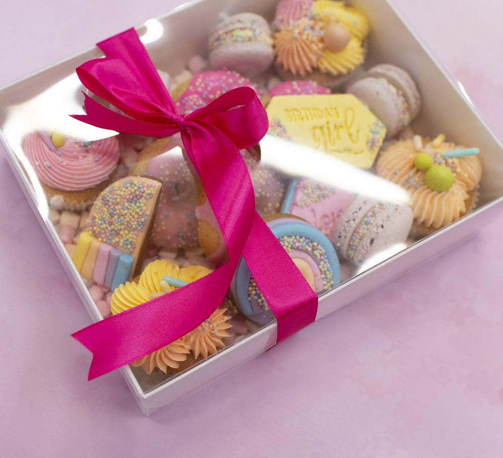 Box of assorted cookies with a pink ribbon on a light purple background