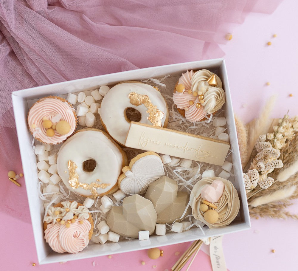 Decorative cookies with gold and pink icing in a box on a pink background