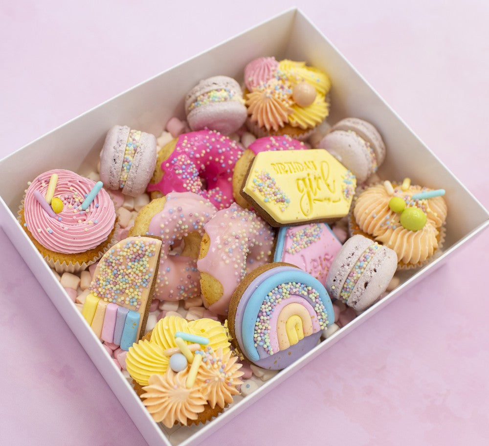 Assorted colorful cookies in a box on a pink background