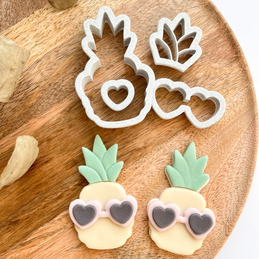 Pineapple-shaped cookie cutters with heart sunglasses on a wooden board