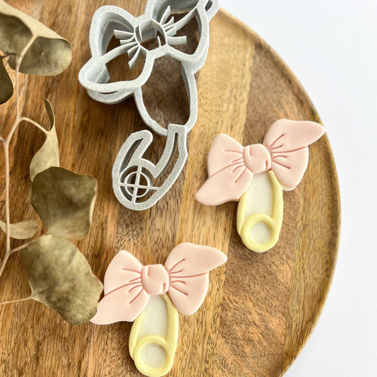 Bow-shaped cookie cutters and cookies on a wooden board with dried leaves.