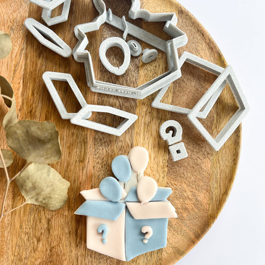 Set of cookie cutters on a wooden board with a decorated cookie resembling a box.