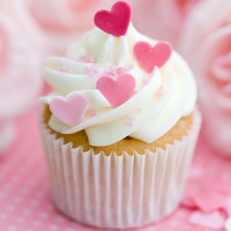 Cupcake with white frosting and pink heart decorations on a pink background