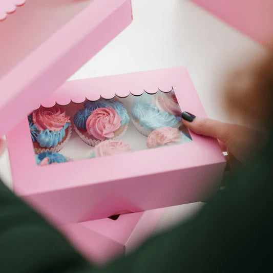 Pink box with decorative items, possibly cupcakes or pastries, held by a person.