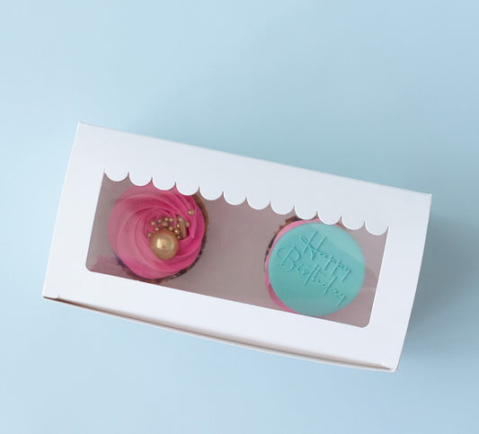 Two cupcakes in a white box with a clear window on a light blue background