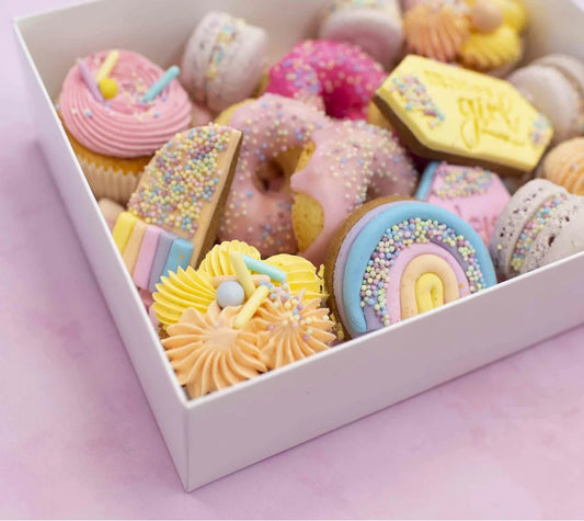 Assorted colorful pastries in a box on a pink background