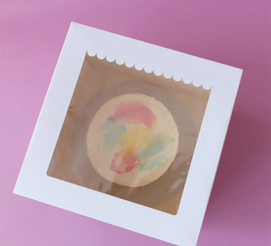 Round bath bomb in a clear window box on a pink background